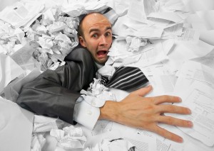 Businessman sinking in heap of documents and asking for help